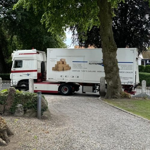 Flyttelastbil parkeret i en grusindkørsel under privatflytning. Klar til transport af møbler og ejendele.