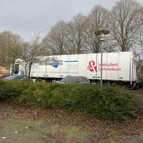 Flyttelastbil parkeret ved flere biler, klar til levering. Effektiv håndtering af flytning fra Haderslev og Vojens flytteforretning.