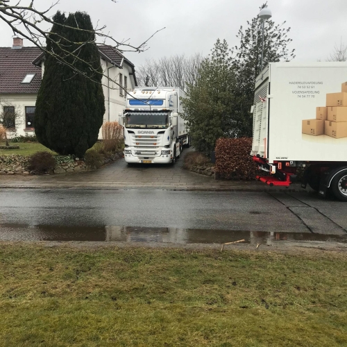 Flyttelastbil parkeret i en indkørsel under en privatflytning på en regnfuld dag. Flyttefirma håndterer flytning effektivt i dårligt vejr.