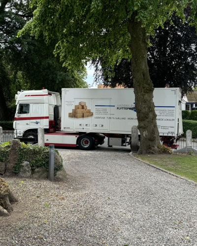 Flyttelastbil parkeret i en grusindkørsel under privatflytning. Klar til transport af møbler og ejendele.